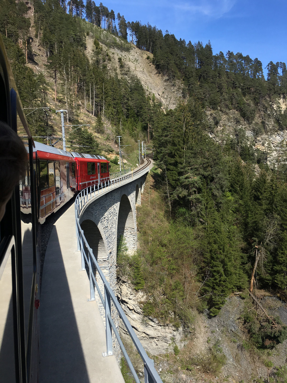 Red panoramic train crossing a stone viaduct through the Swiss Alps